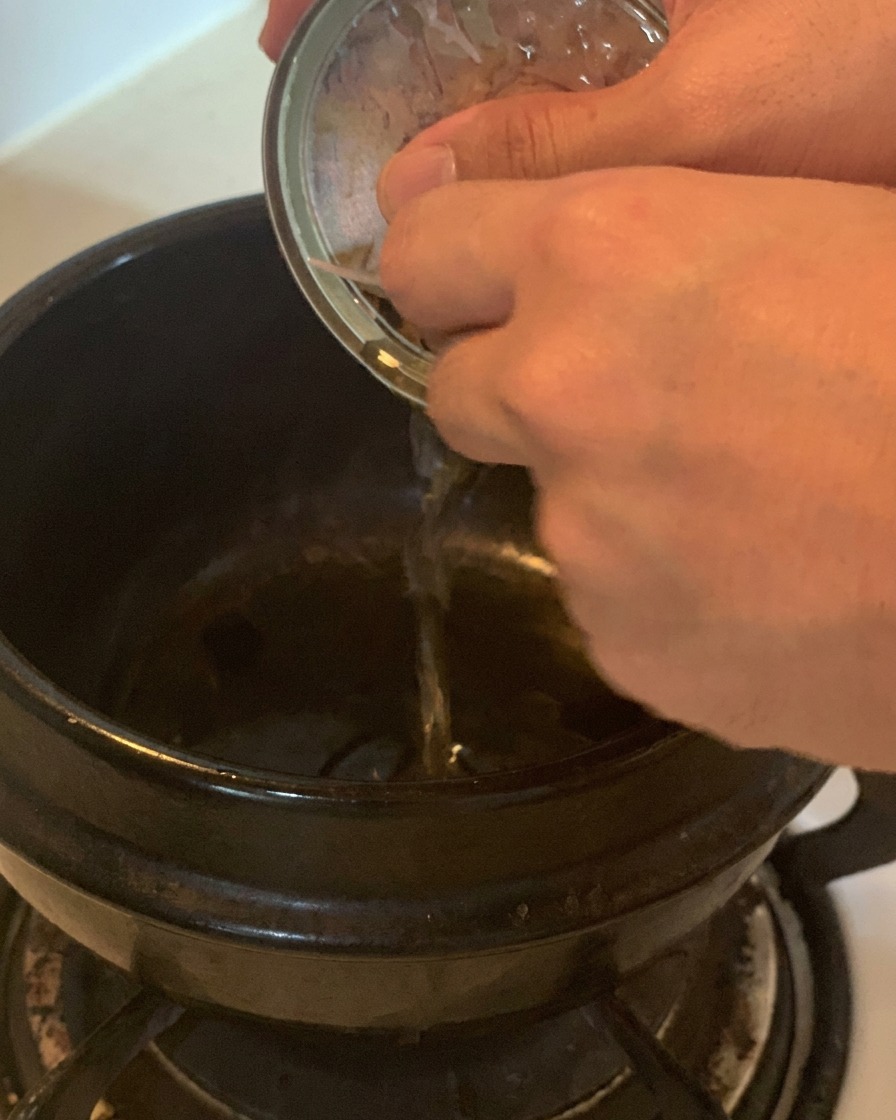 가스레인지 위 검은색 냄비에 참치캔 속 기름을 따라 붓는 모습.
