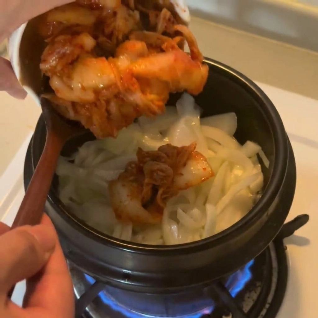 볶은 양파 위에 송송 썬 빨간 김치를 넣는 모습.
