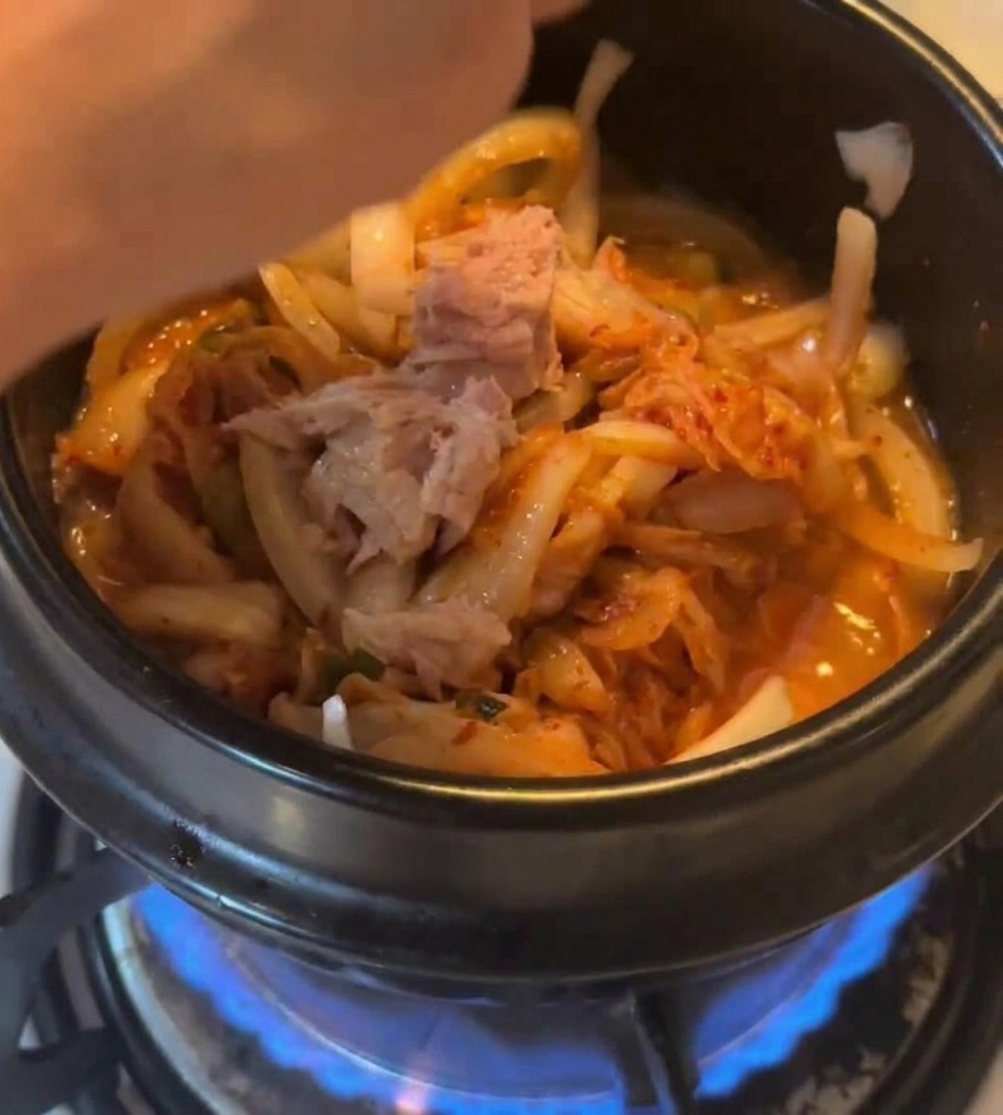 김치를 볶던 냄비에 참치 살코기 덩어리를 통째로 넣는 모습.