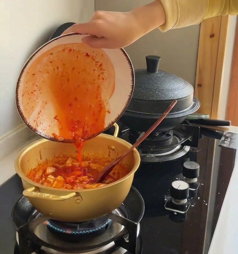 볶은 김치가 담긴 냄비에 진한 김치 국물을 붓는 장면