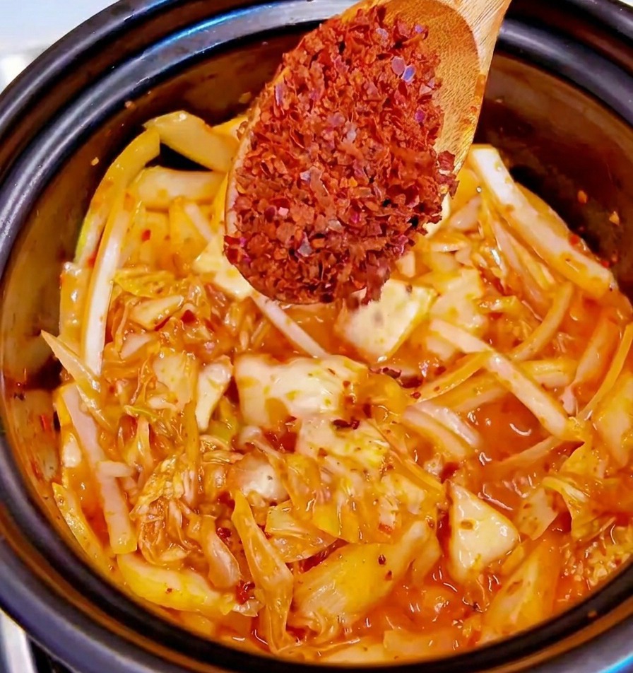 볶아지는 재료 위에 굵은 고춧가루를 한 스푼 뿌리는 모습