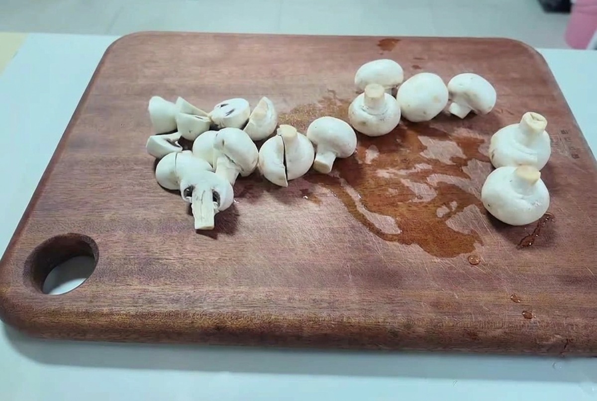 어두운 나무 도마 위에서 신선한 양송이버섯을 두툼하게 썰고 있는 모습.