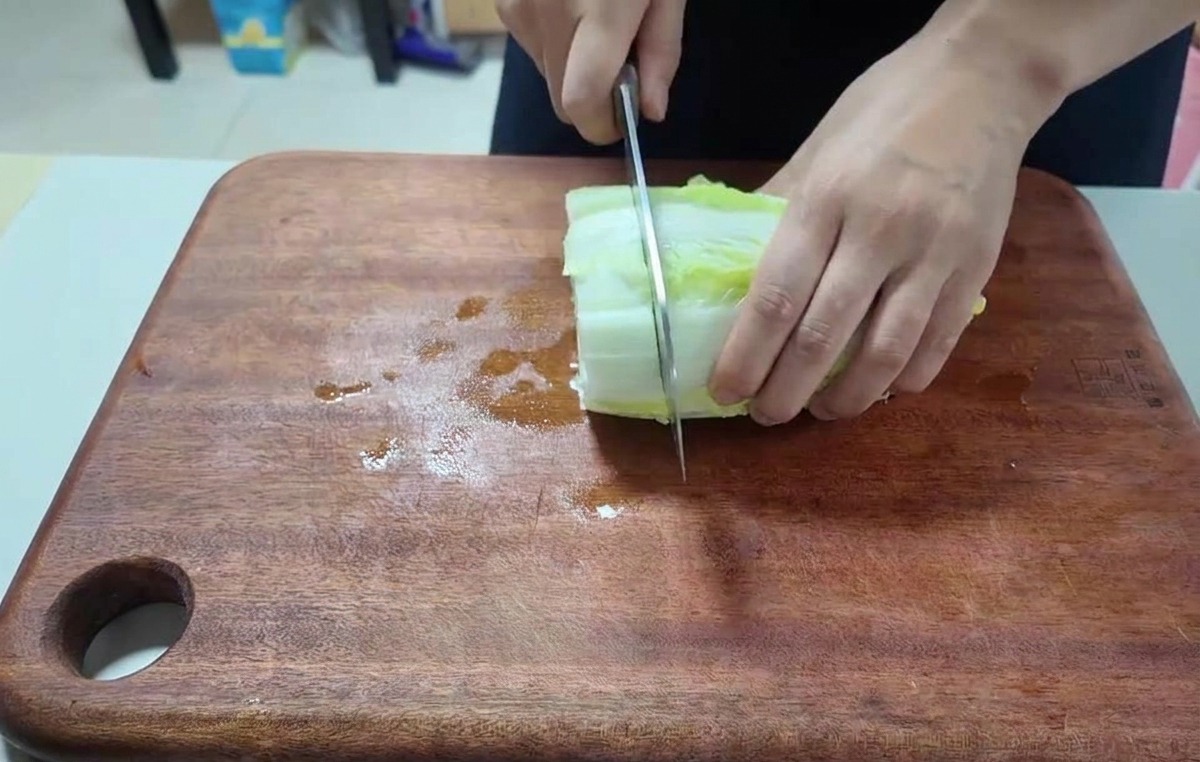 어두운 도마 위에서 알배기 배추 잎을 큼직하게 썰고 있는 클로즈업 사진.