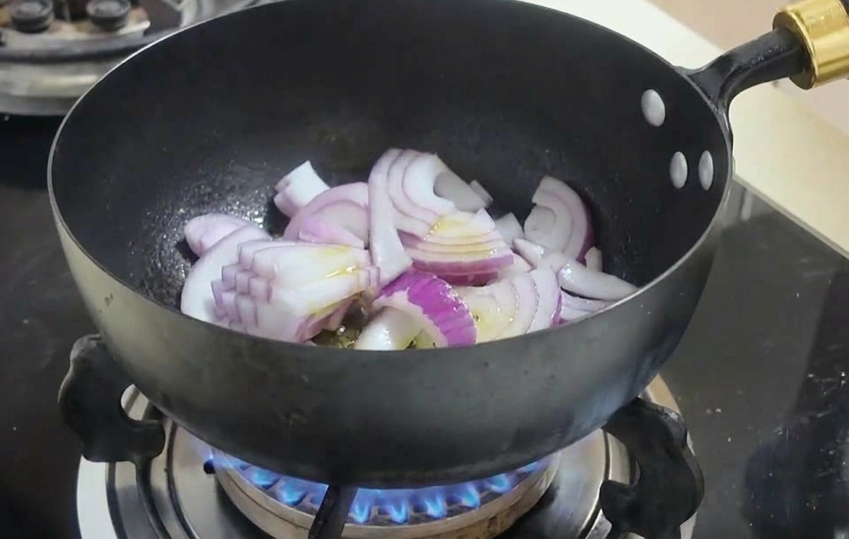 검은색 웍 안에서 썰어둔 적양파가 노릇하게 볶아지고 있는 모습.