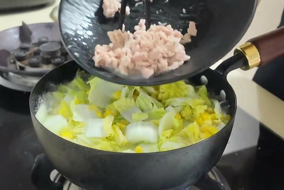 젓가락을 이용해 캔참치를 끓는 채소 찌개 속으로 넣고 있는 모습.