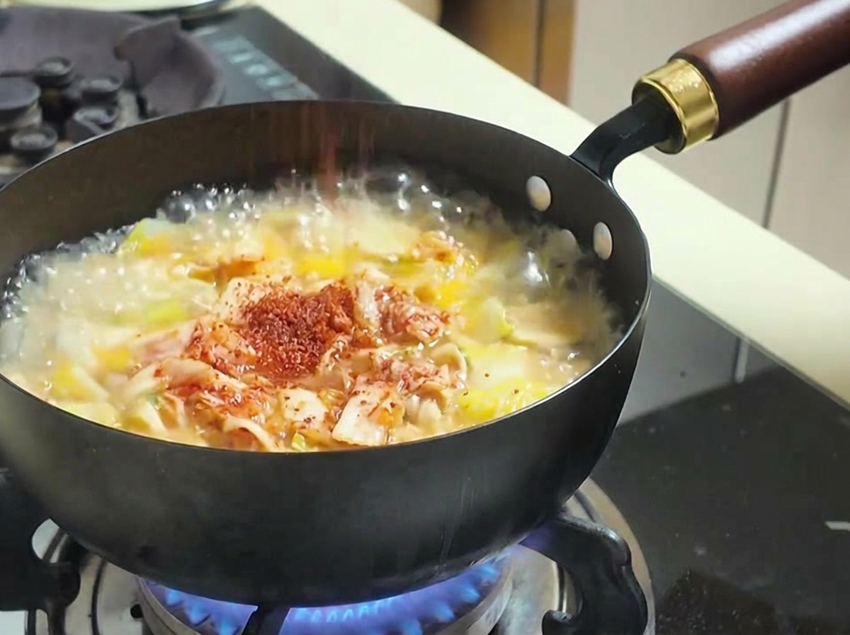 보글보글 끓는 김치찌개 위에 붉은 고춧가루를 솔솔 뿌리는 모습.