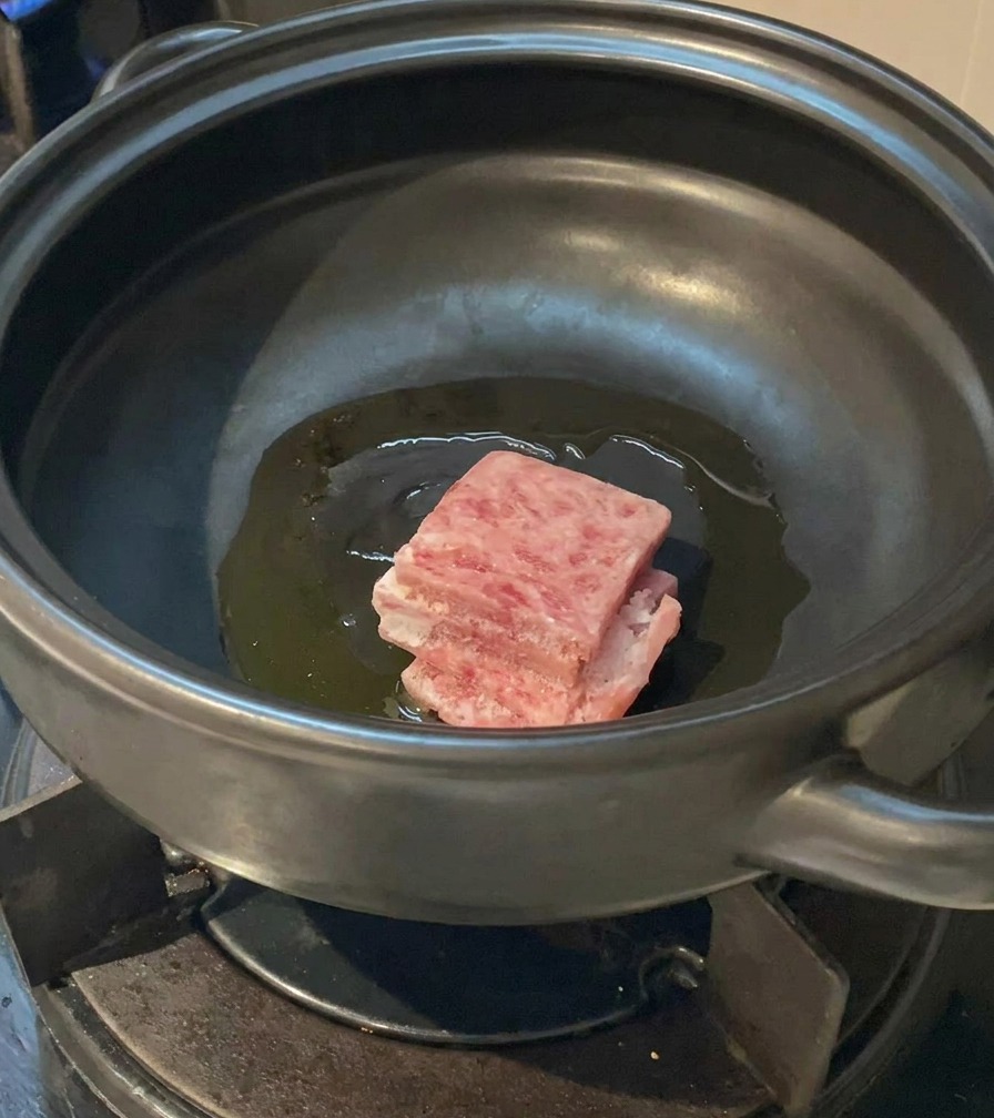 달궈진 기름이 있는 뚝배기에 선홍빛 삼겹살 조각들을 넣는 모습.