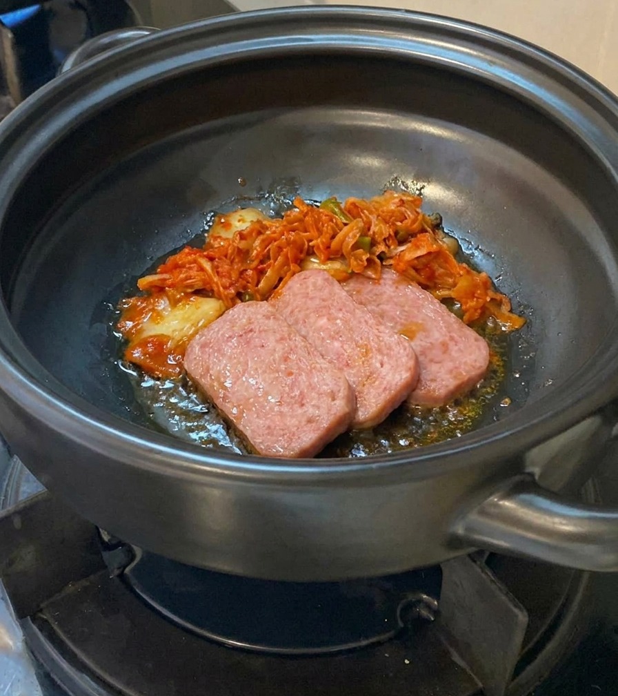 고기가 익어가는 뚝배기에 잘게 썬 김치를 추가하는 장면.