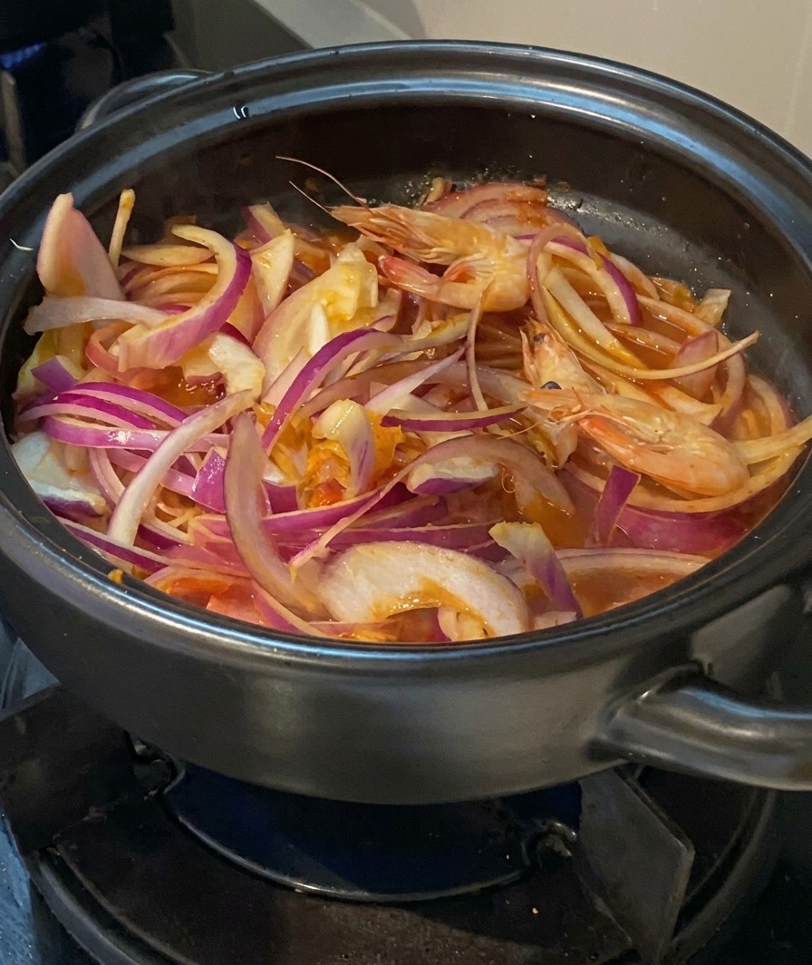 양파, 김치, 고기가 담긴 뚝배기에 머리가 달린 신선한 통새우를 넣는 모습.