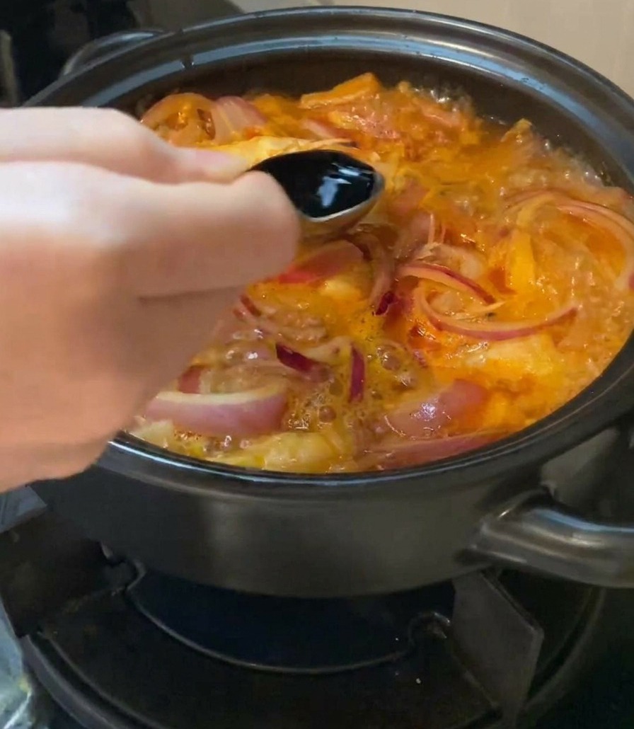 보글보글 끓는 김치찌개에 숟가락으로 국간장을 넣고 있는 모습.