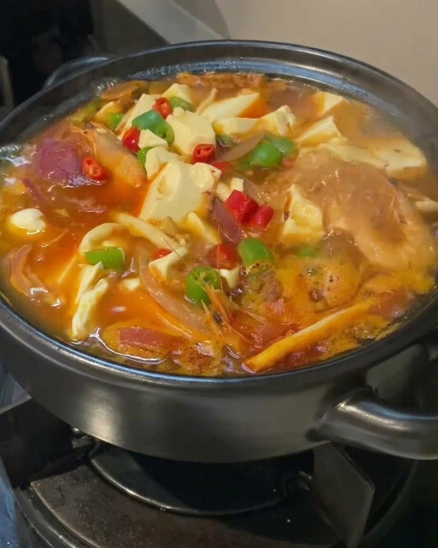 두부와 고추 고명이 올라간 채 보글보글 끓고 있는 김치찌개의 클로즈업.
