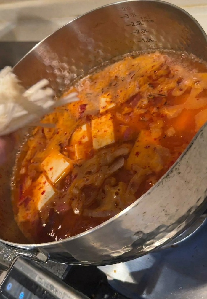 순두부가 들어있는 끓는 냄비에 팽이버섯 묶음을 넣는 모습