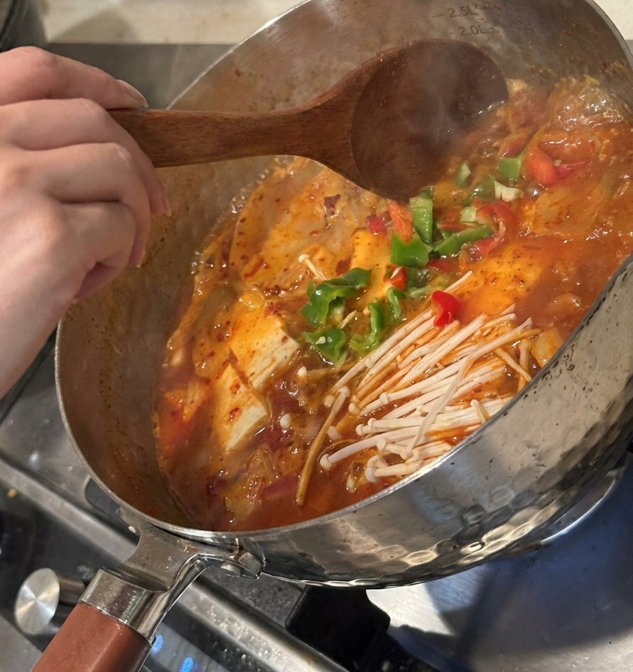 썰어둔 고추와 김치를 냄비에 넣고 나무 주걱으로 섞는 모습