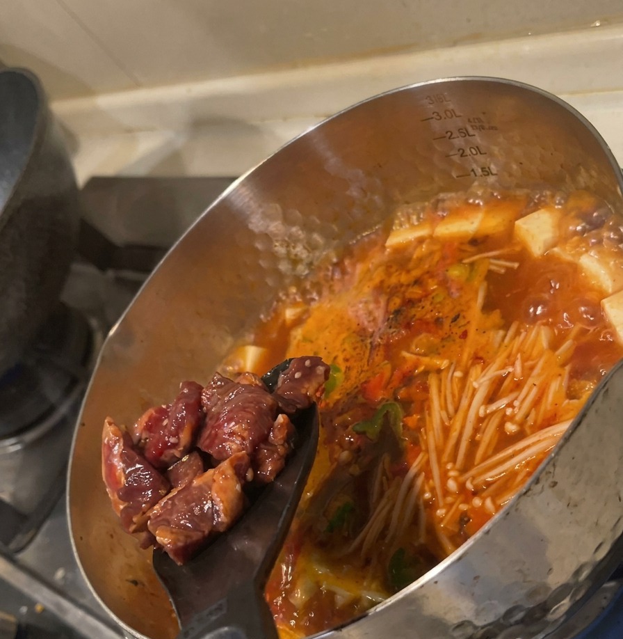 검은색 뒤집개로 양념된 소고기를 끓는 국물에 밀어 넣는 모습