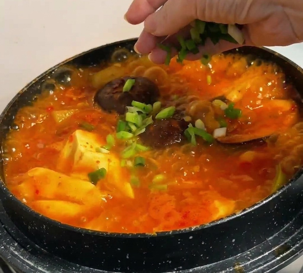 완성된 순두부찌개 위에 대파와 고추를 뿌리는 모습.