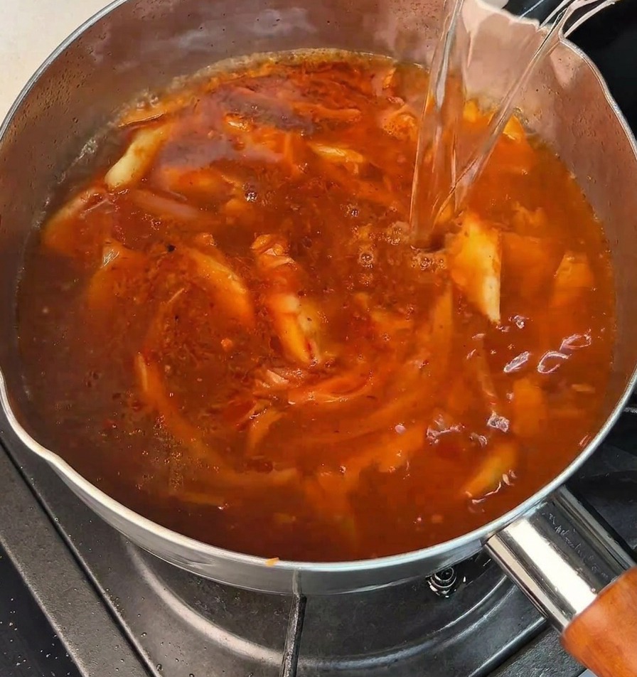 끓는 물이 냄비 속 보글보글 끓는 빨간 양념 베이스에 부어지는 모습