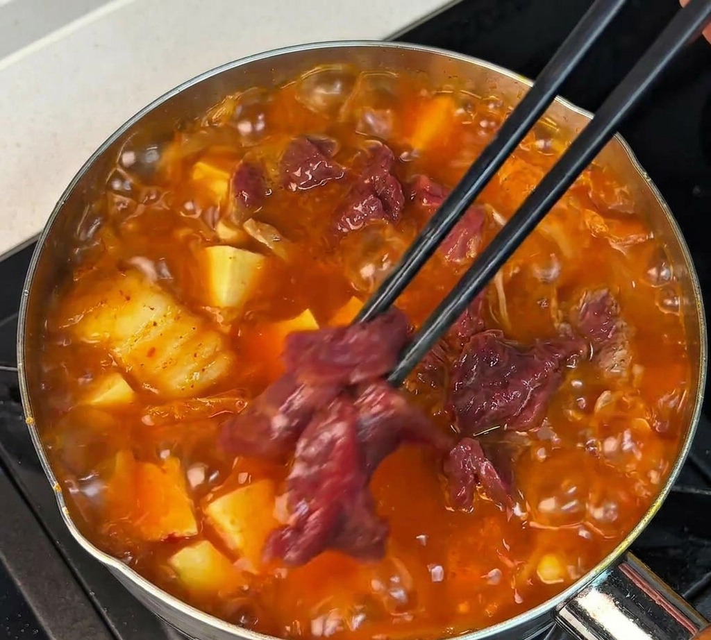 끓는 국물에 양념된 소고기를 젓가락으로 하나씩 넣고 있는 모습