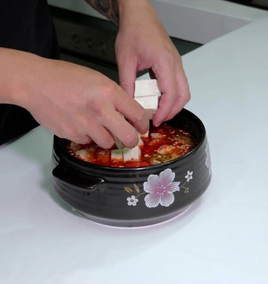 붉은 국물 베이스 위에 흰 두부와 대파를 올리는 모습.