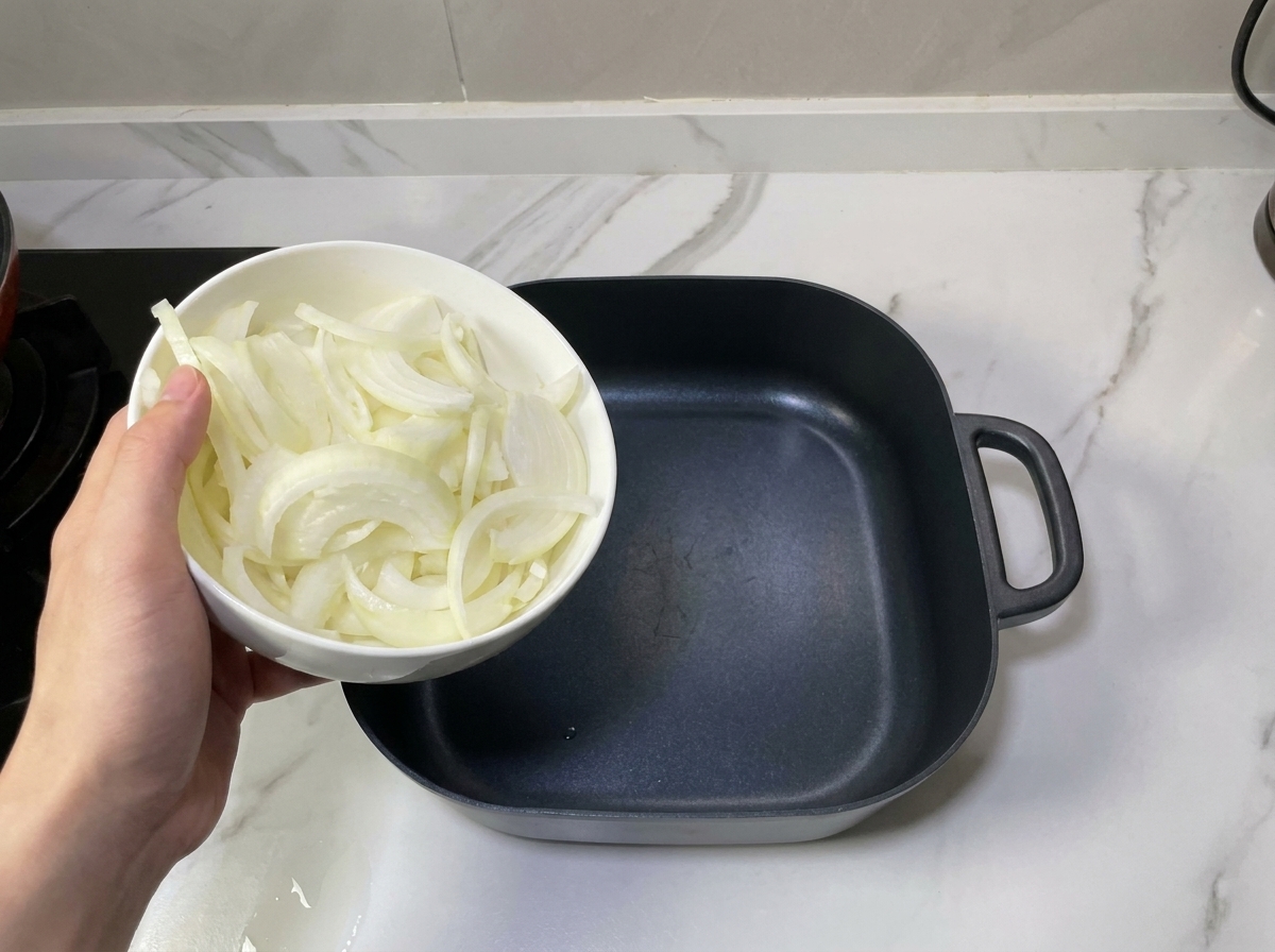 빈 검정색 전골 냄비 바닥에 얇게 썬 양파를 담고 있는 모습.