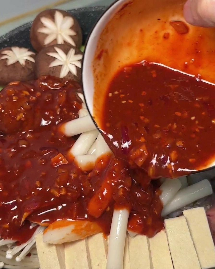 준비된 재료 위에 매콤한 빨간 양념장을 끼얹는 모습
