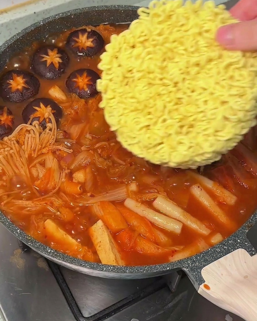 끓는 찌개 중앙에 라면 사리를 넣고 있는 모습
