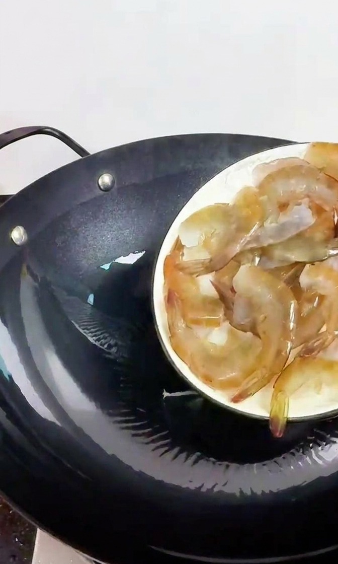달궈진 검은색 무쇠 웍에 신선한 생새우를 넣는 모습