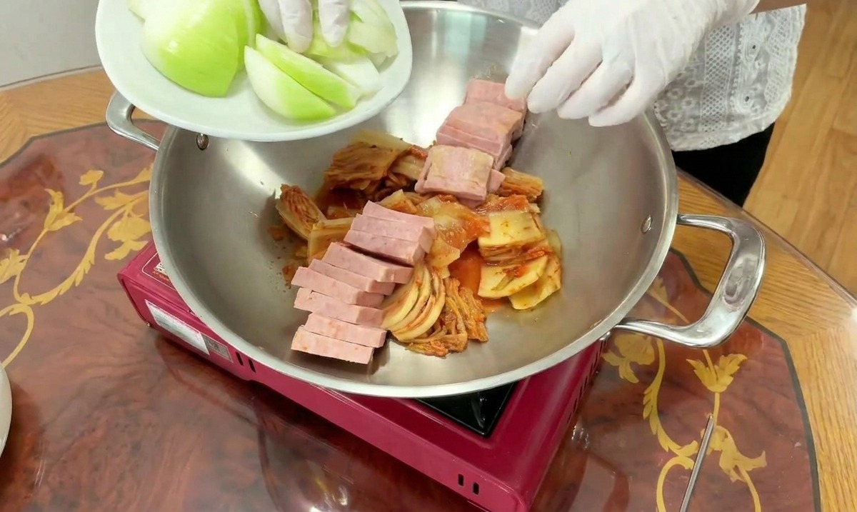 김치와 스팸이 담긴 냄비에 큼직하게 썬 양파를 채워 넣는 모습.