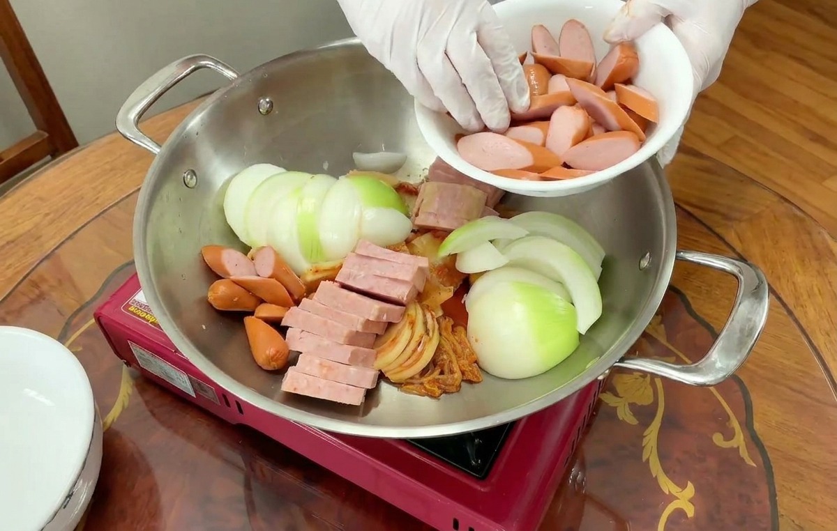 양파, 햄, 김치가 담긴 냄비의 빈 곳에 어슷 썬 소시지를 채워 넣는 모습.
