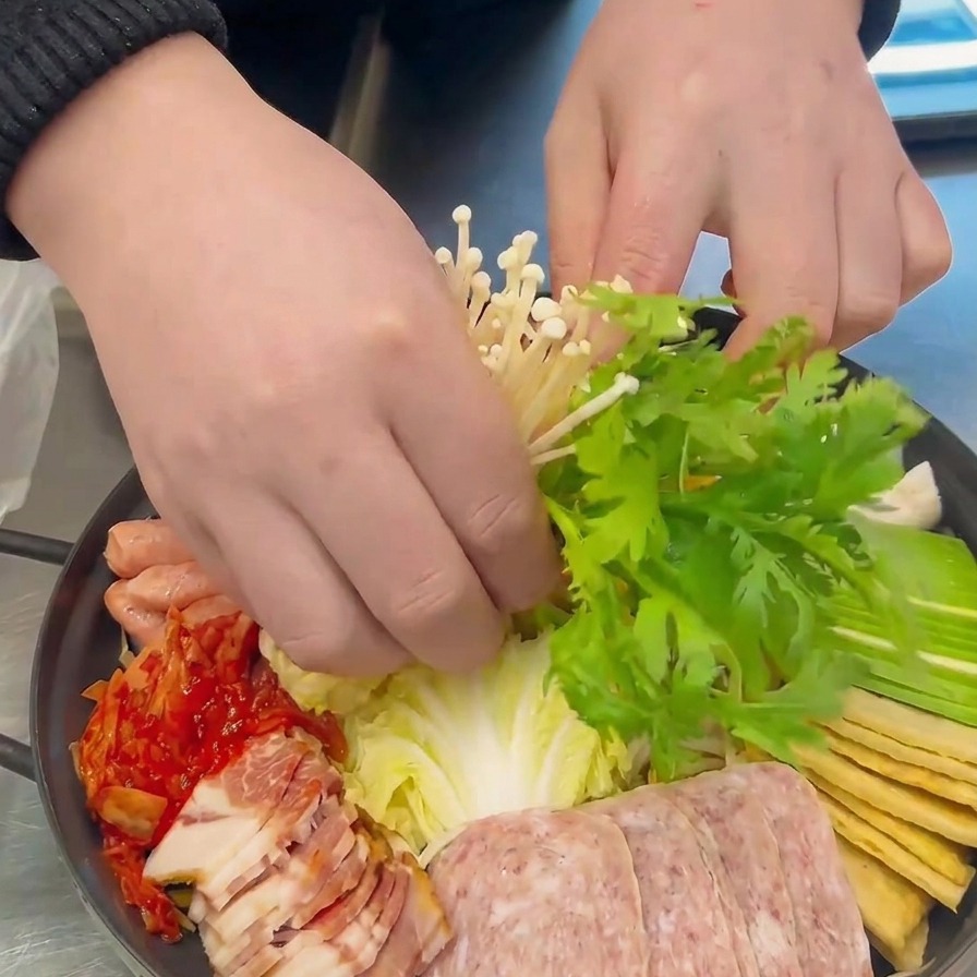 준비된 냄비 중앙에 팽이버섯 뭉치와 초록색 쑥갓을 조심스럽게 올리는 모습.
