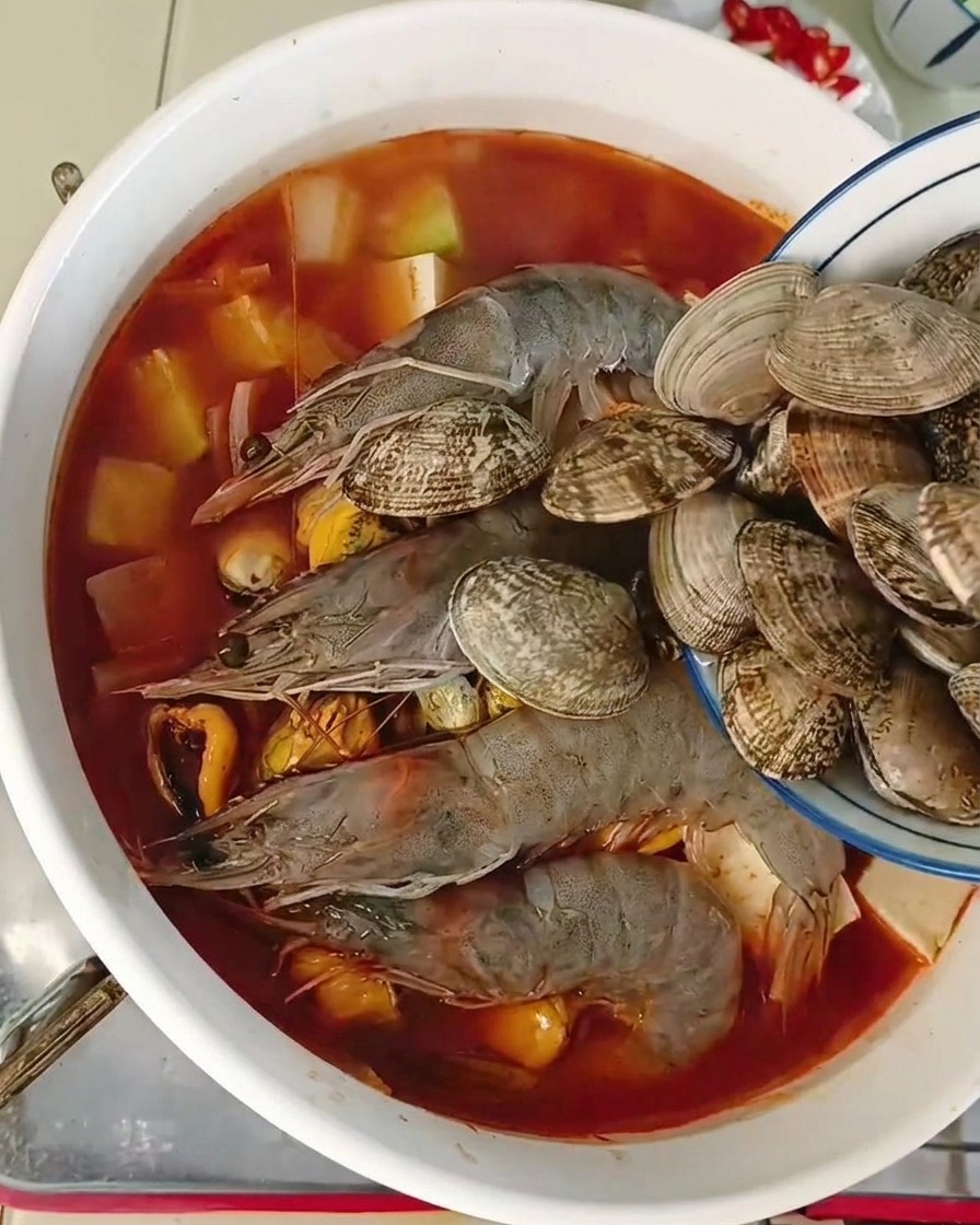 새우와 두부가 들어있는 냄비에 생조개를 마지막으로 넣는 모습