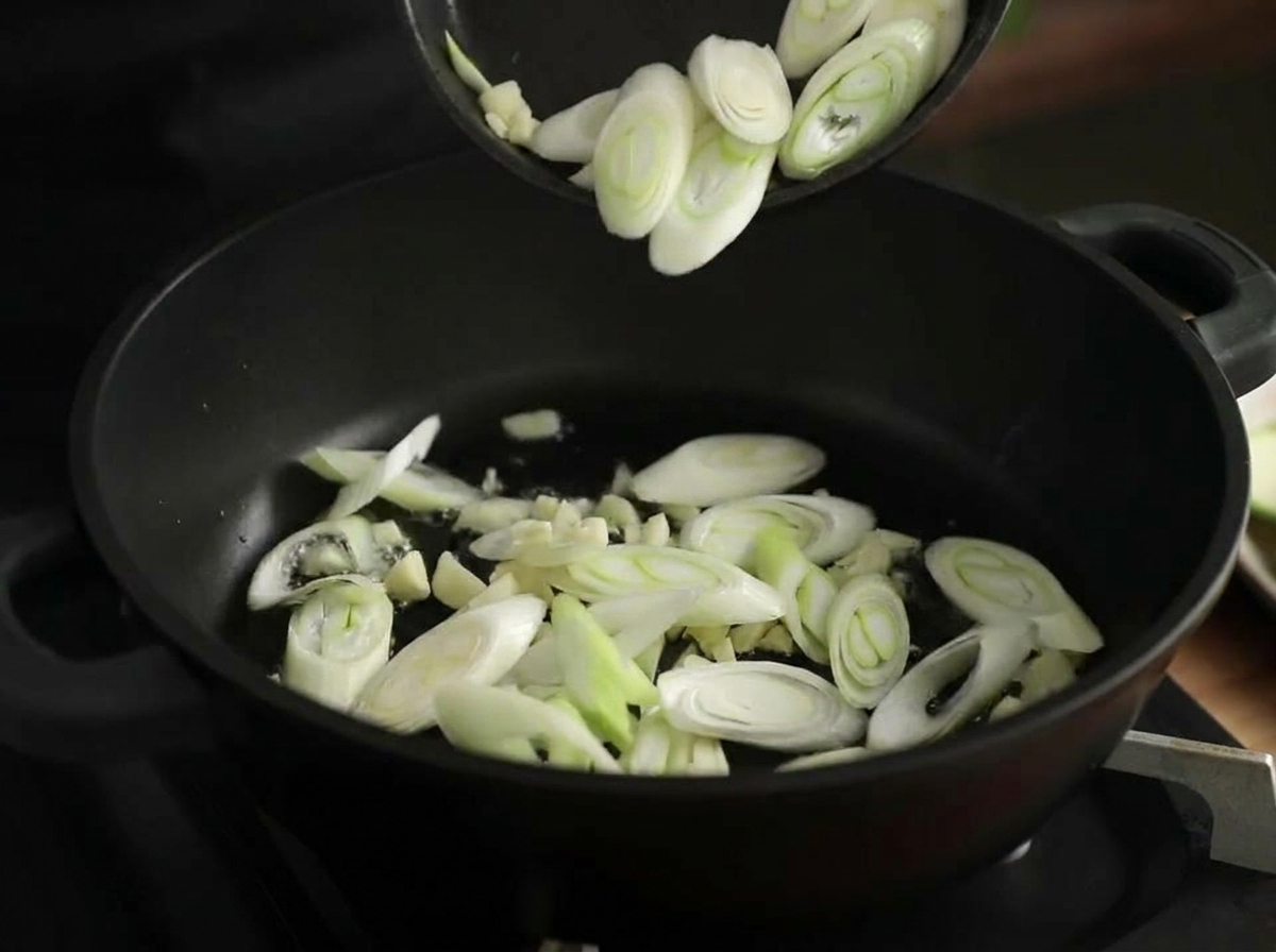 검은 냄비에 기름을 두르고 다진 마늘과 대파를 함께 볶는 모습.