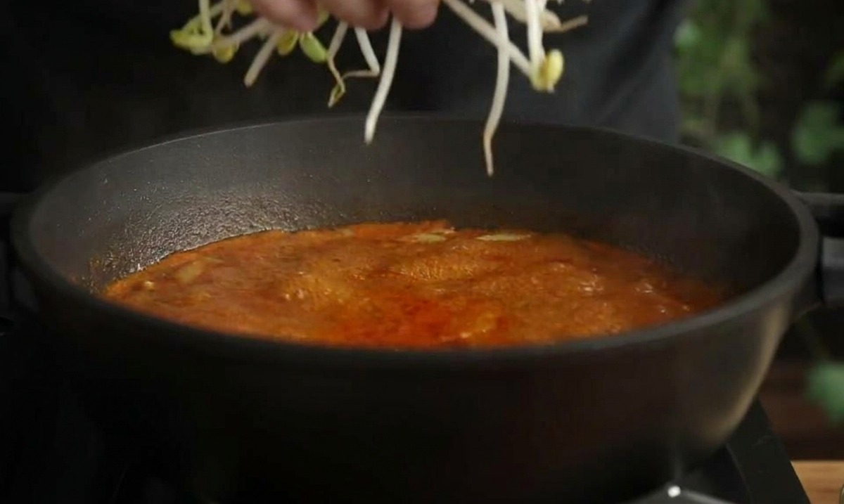 끓는 빨간 찌개 국물에 신선한 콩나물을 한 줌 넣는 손.