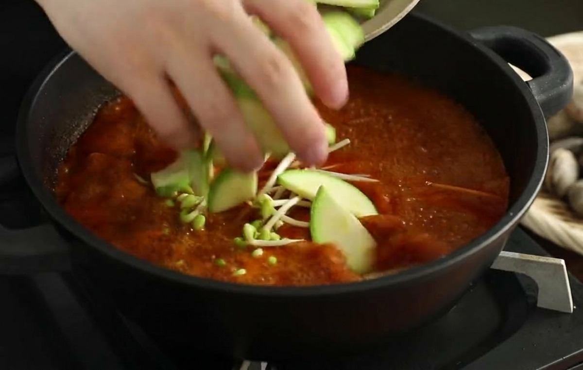 콩나물이 든 찌개에 반달 모양 애호박을 넣는 모습.