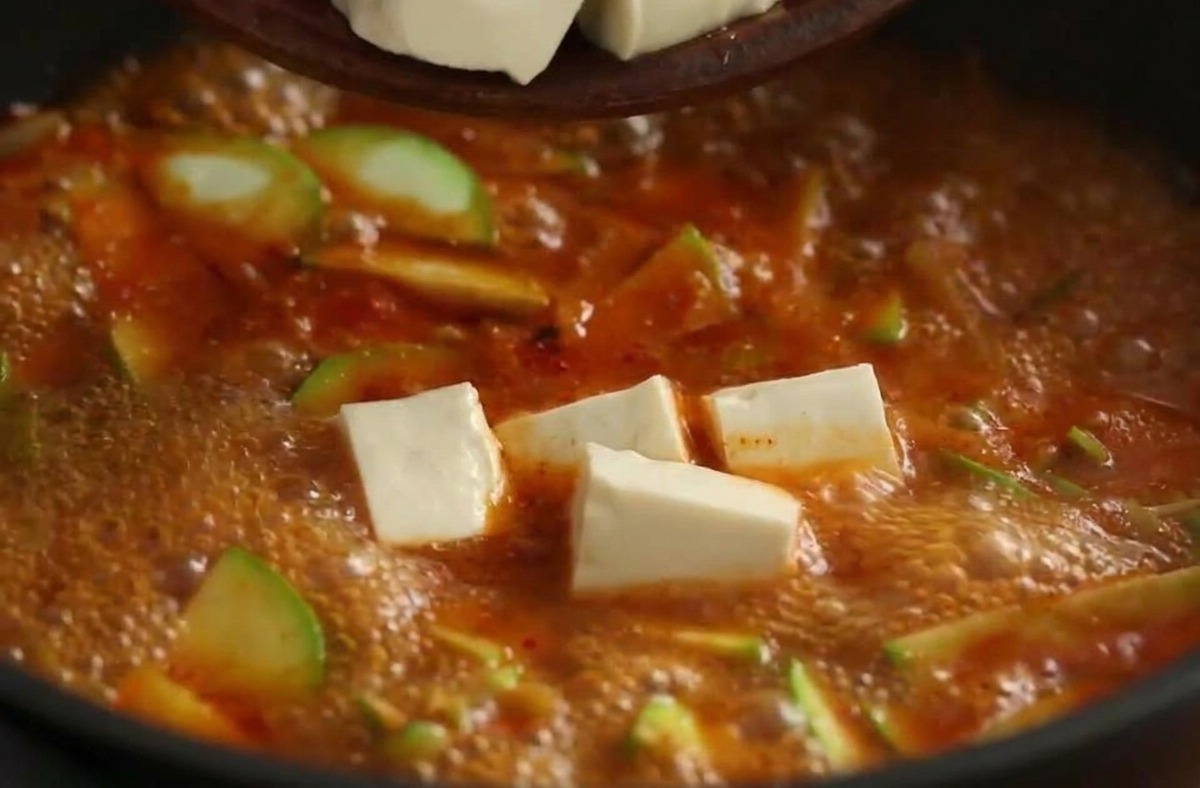 하얀 두부 큐브를 끓어오르는 해물 찌개에 조심스럽게 넣는 모습.