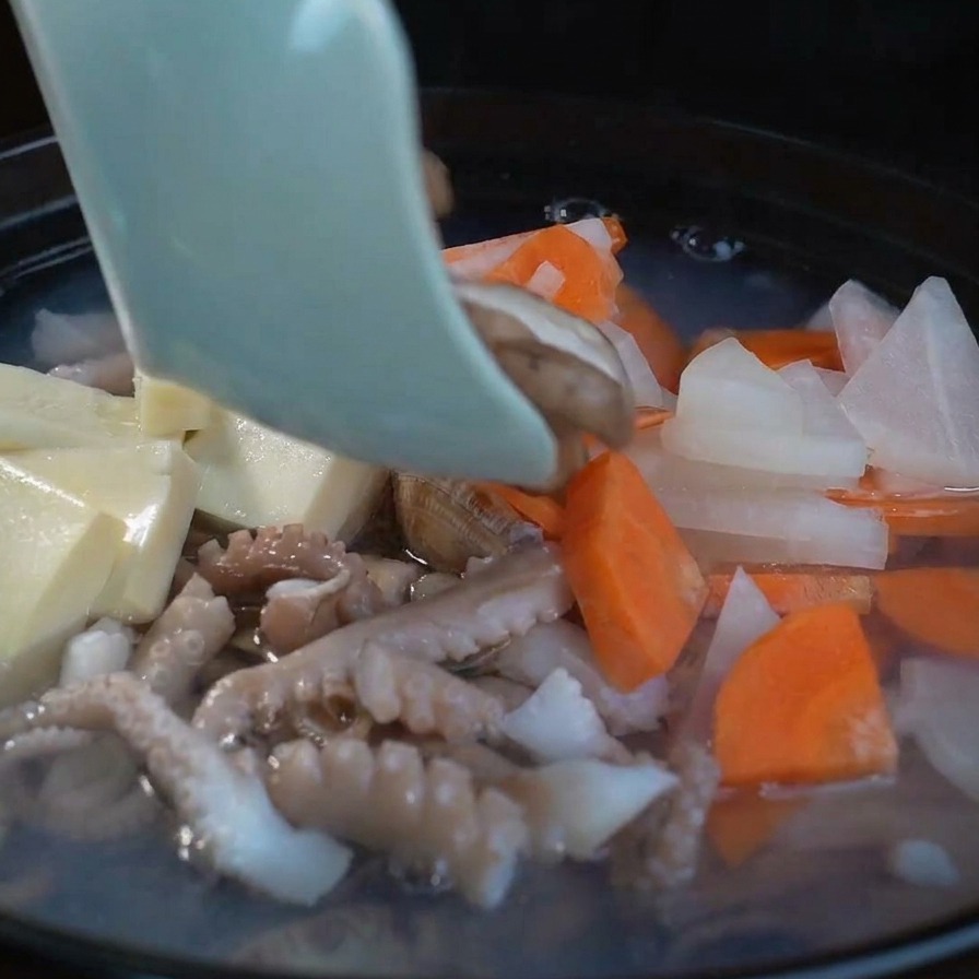 보글보글 끓는 찌개 위에 표고버섯 슬라이스를 올리는 모습.