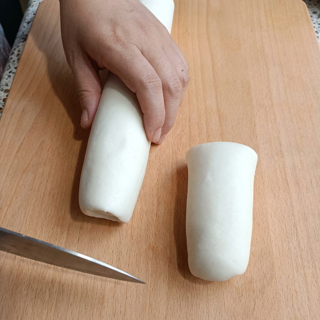 나무 도마 위에서 길쭉한 흰색 반죽을 칼로 등분하여 자르는 손.