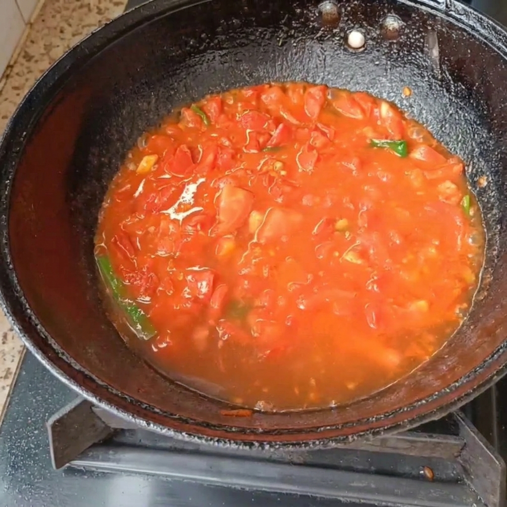 가스레인지 위 검은색 웍에서 토마토와 대파가 물과 함께 끓고 있는 모습.