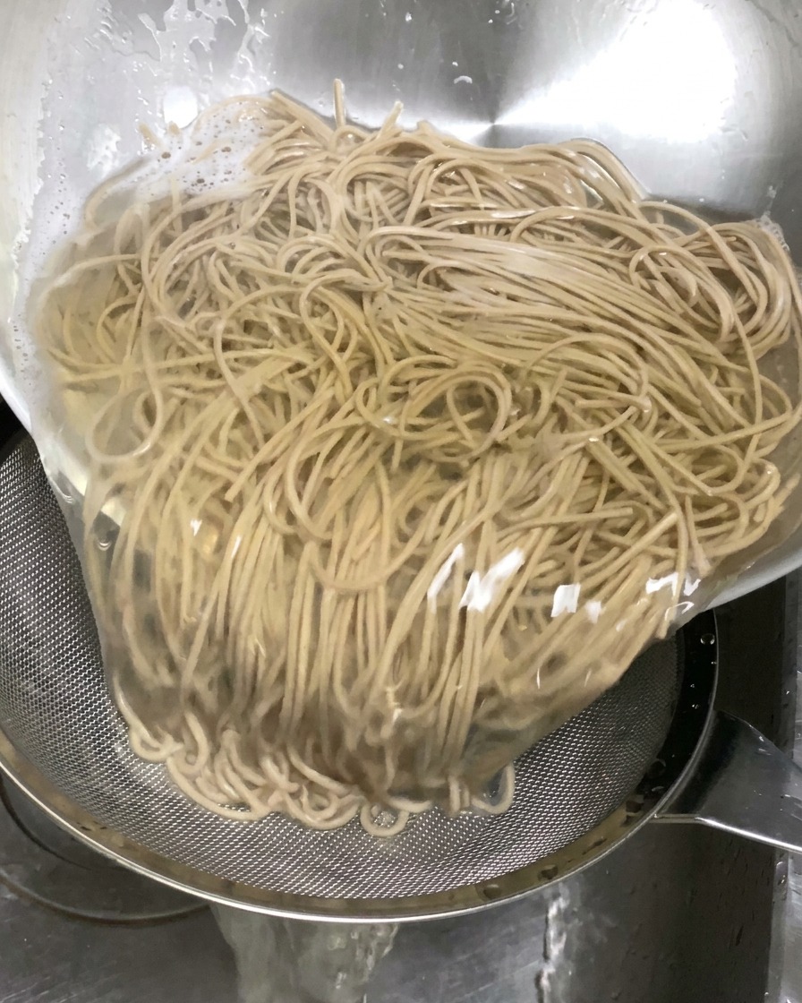 삶은 메밀면을 체에 받쳐 찬물에 헹구는 모습.