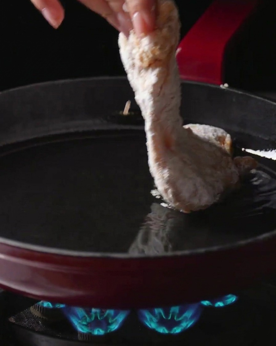 가스 불 위에 올려진 뜨거운 기름 팬에 가루를 묻힌 닭다리살을 조심스럽게 넣는 모습.