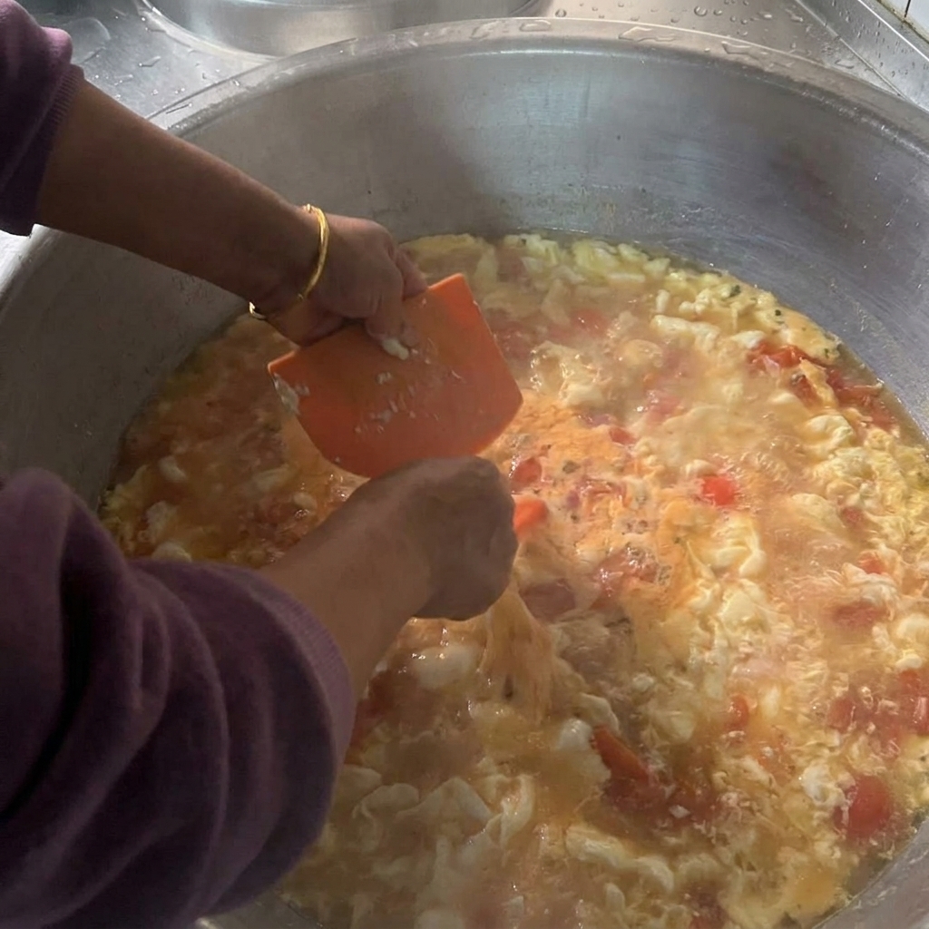 주황색 플라스틱 스크래퍼를 사용하여 끓고 있는 토마토 국물에 진 반죽을 조금씩 떼어 넣는 손.