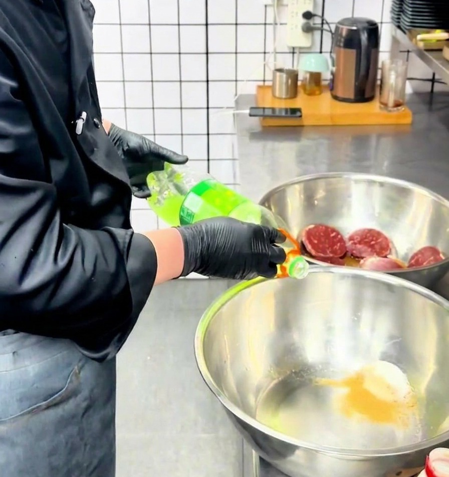셰프가 조미료 가루가 담긴 스테인리스 믹싱 볼에 투명한 초록색 액체를 병에서 따르는 모습.