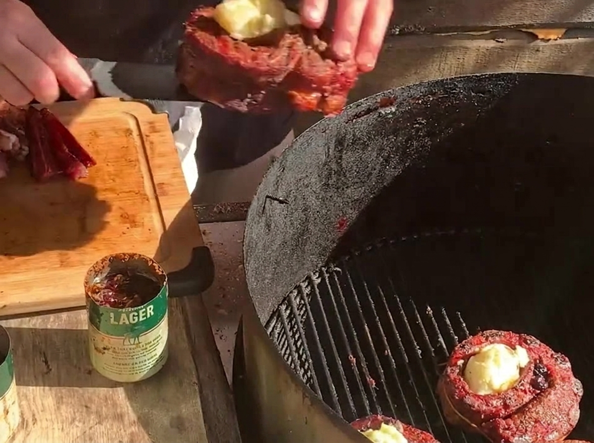감자를 채운 립 컵을 다른 고기 컵 및 두껍게 썬 베이컨과 함께 숯불 그릴 위에 다시 올리는 모습.