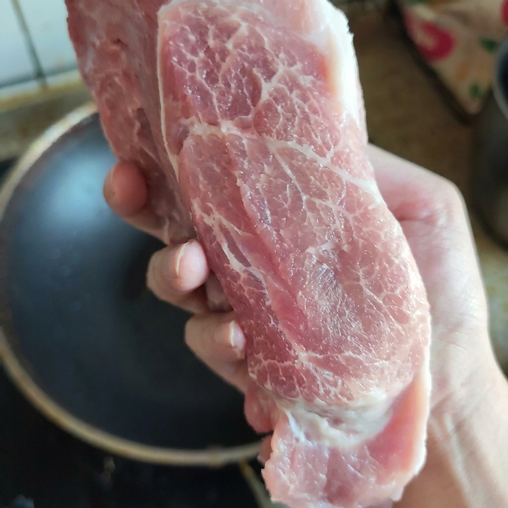 손으로 들어 올려 신선한 육질과 고른 마블링 상태를 보여주는 생 돼지고기 목살 부위