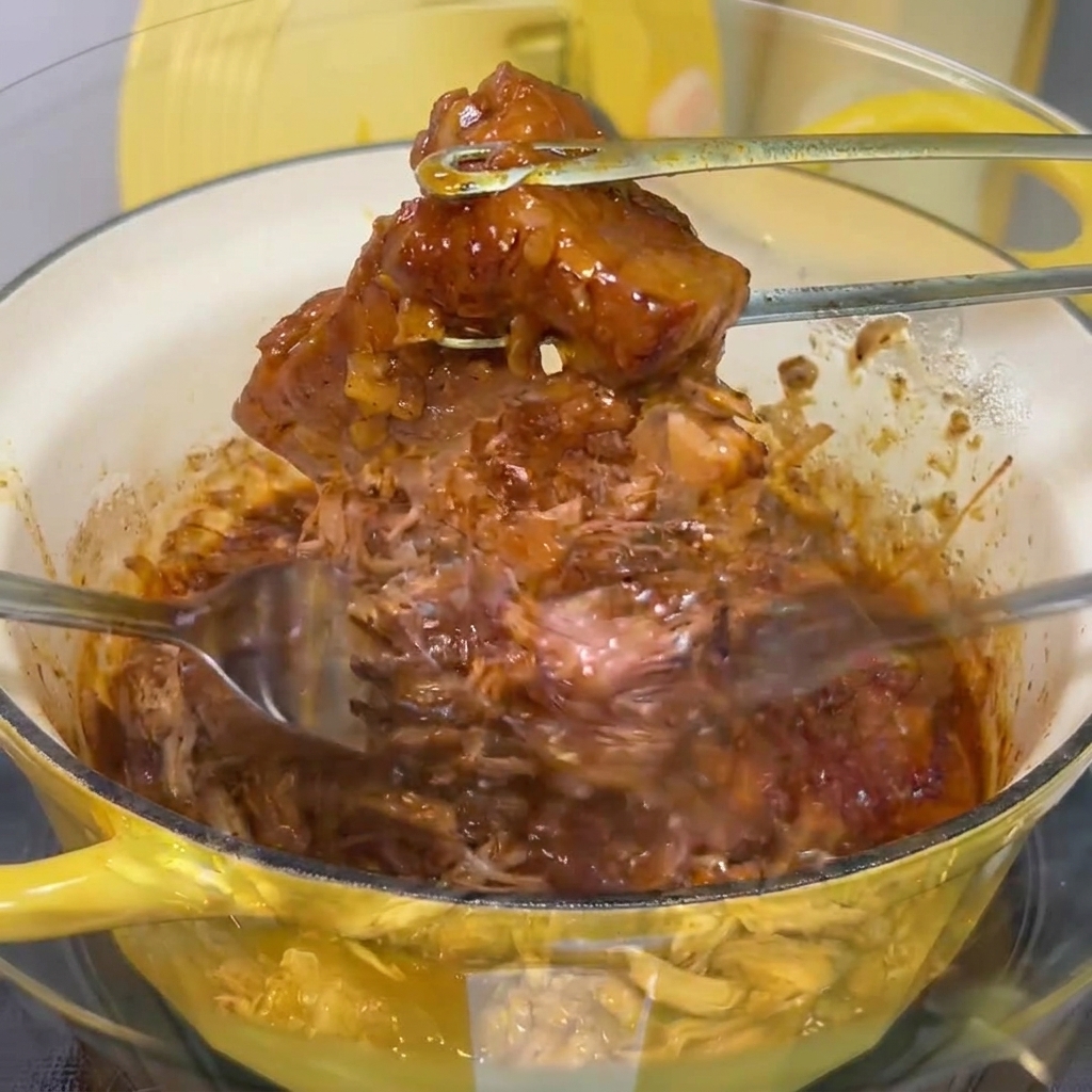 유리 볼에 담긴 부드러운 고기를 포크 두 개를 사용해 잘게 찢는 모습.
