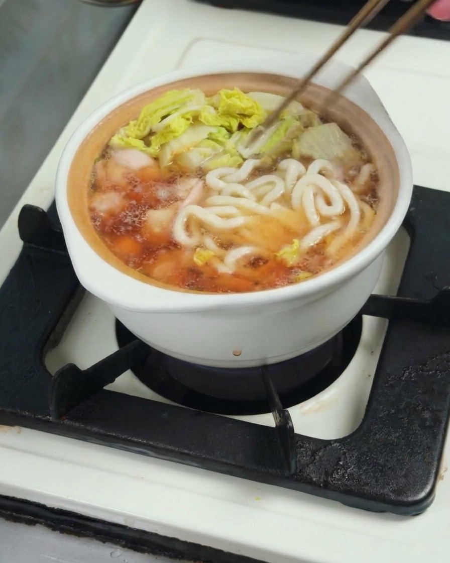 육수와 닭고기, 청경채가 담긴 냄비에 우동 면을 넣는 모습.