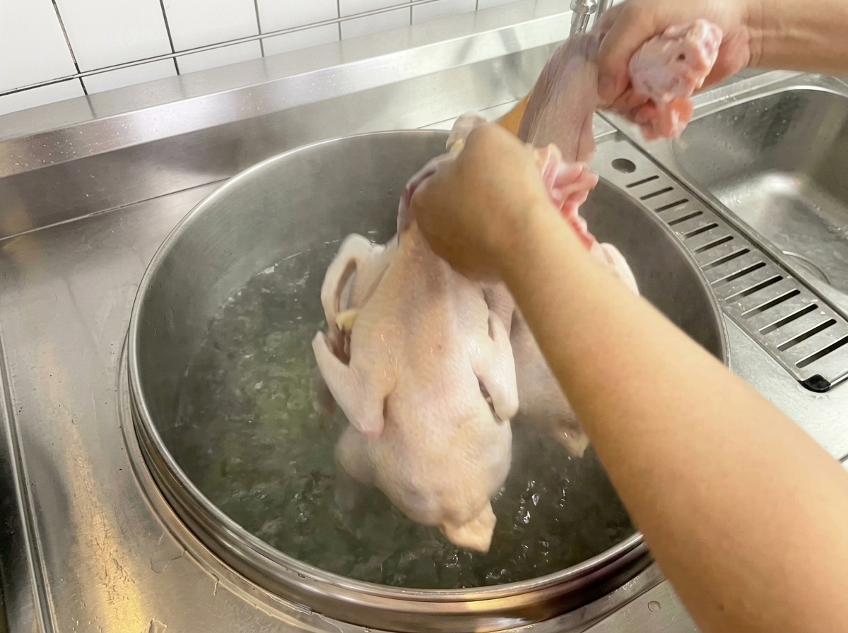 끓는 물이 담긴 큰 냄비에 닭을 담그고 있는 모습.