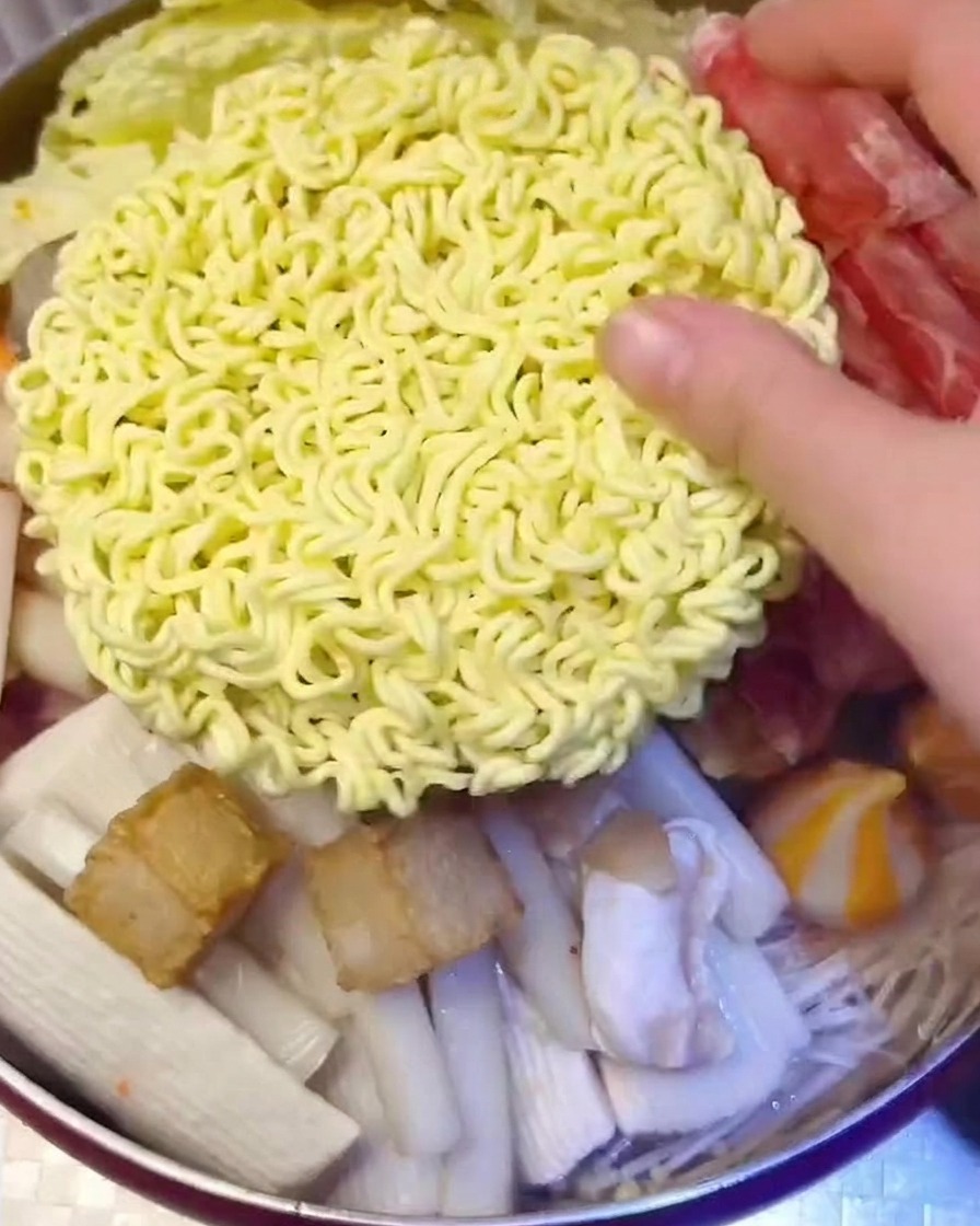 냄비 중앙에 라면 사리와 치즈 슬라이스를 올리는 모습.