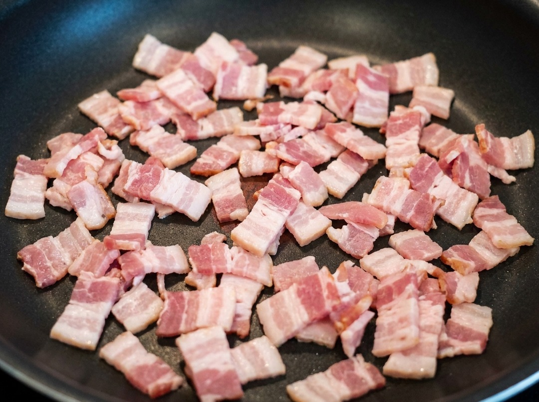 팬에서 베이컨 조각이 볶아지며 기름이 나오는 모습.