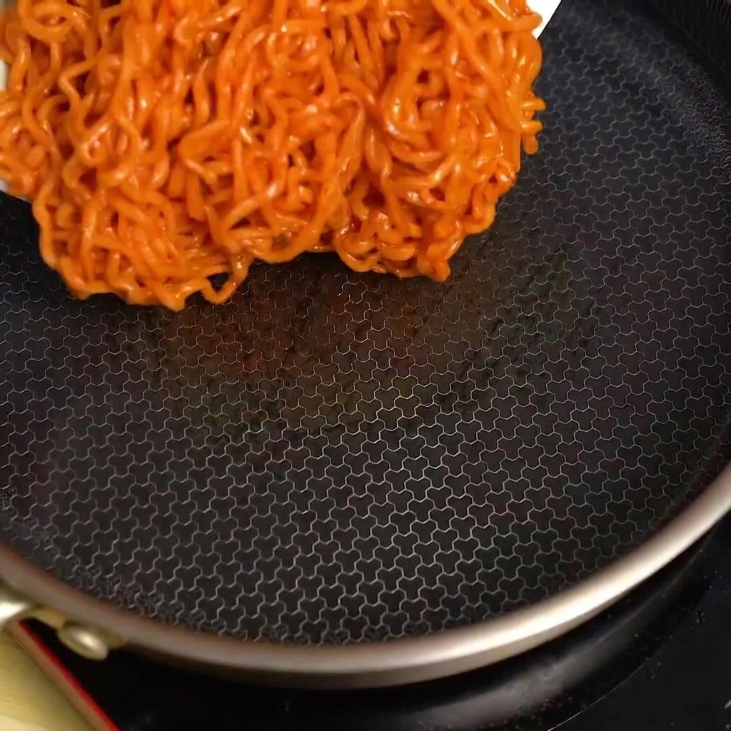 뜨겁게 달궈진 검은색 프라이팬에 불닭볶음면을 붓는 모습.