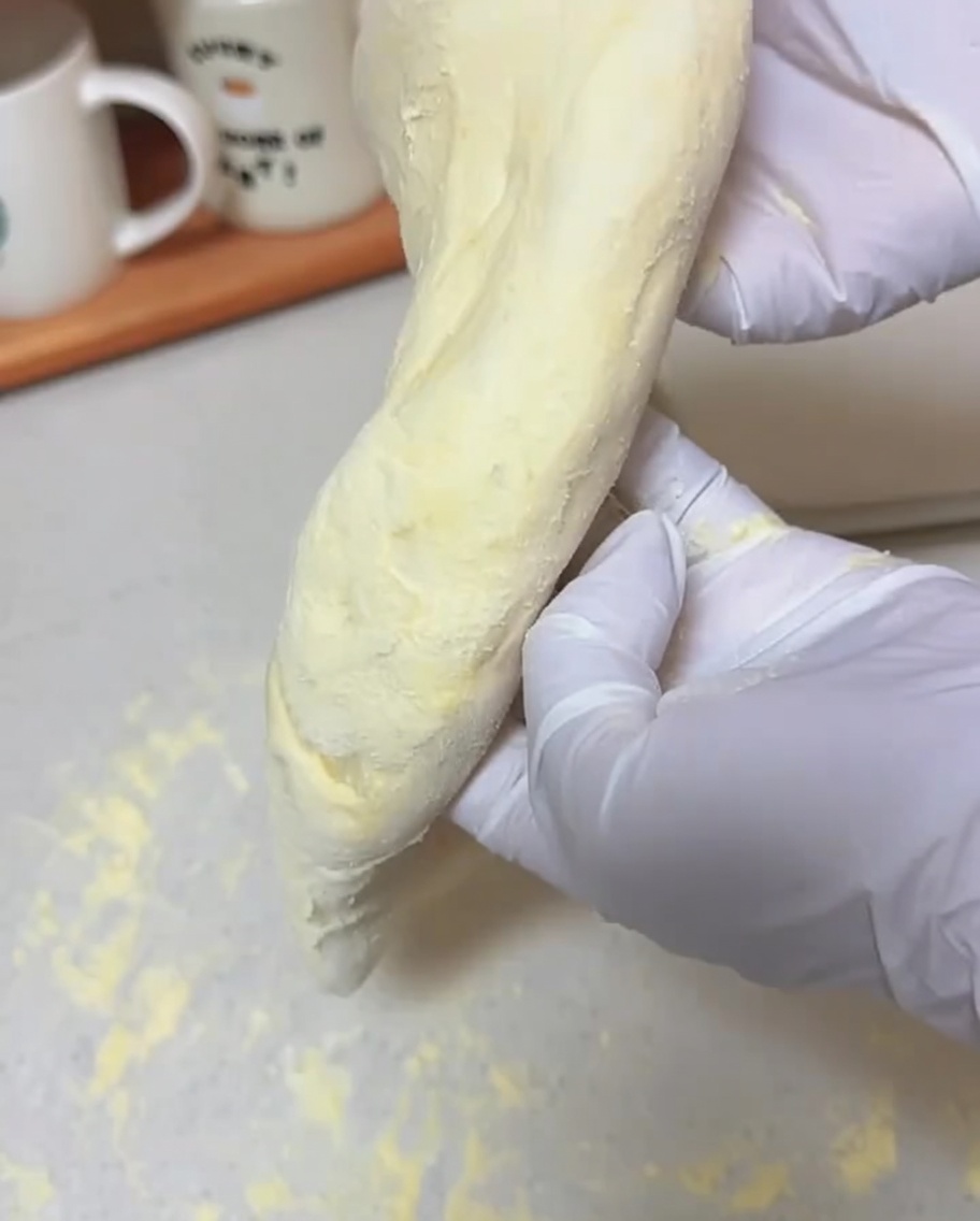 장갑을 낀 손이 부드러운 반죽을 수직으로 들고 얇은 피자 도우 모양으로 늘어지게 하는 모습입니다.